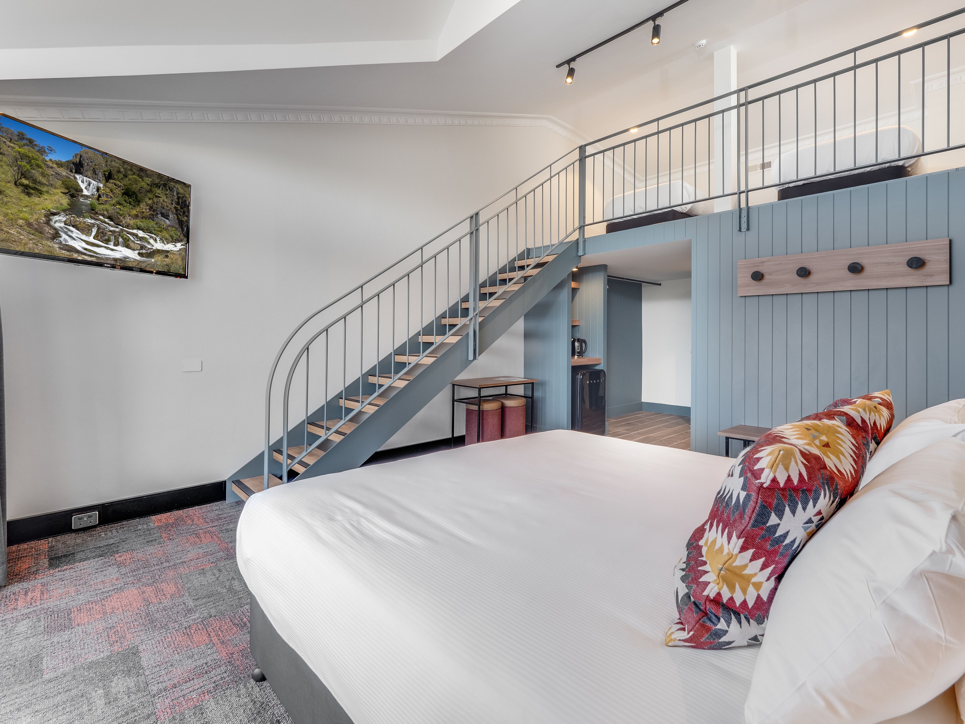 A bedroom with a large bed, a staircase, a small kitchenette, and a large window with a waterfall view.