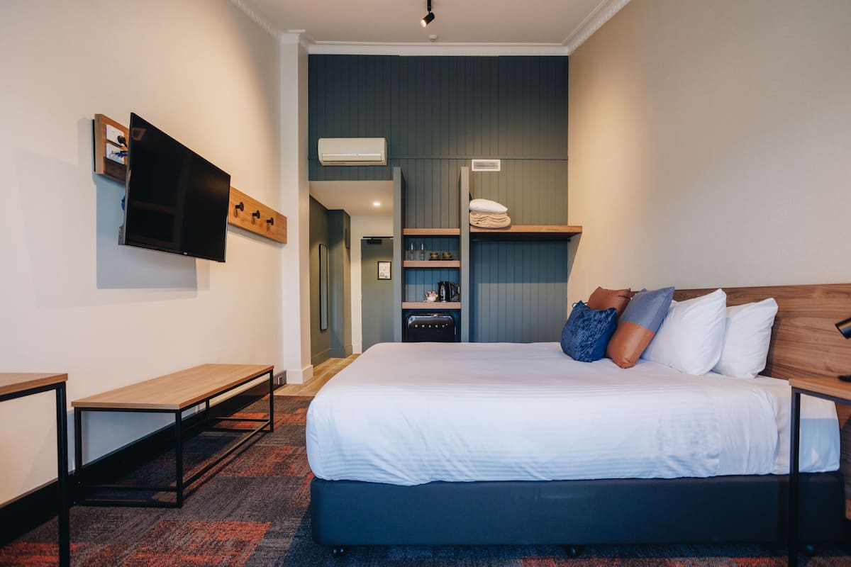 Una habitación de hotel moderna con una cama grande, un televisor de pantalla plana en la pared, un escritorio pequeño y un estante empotrado con artículos de tocador.