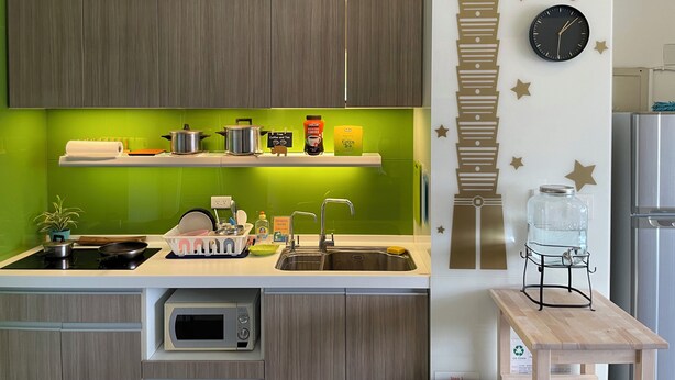 A modern kitchen with wooden cabinets, a green backsplash, and a wall clock. - Easymind Guesthouse, Hostel in Taipei Main Station (Taipei)