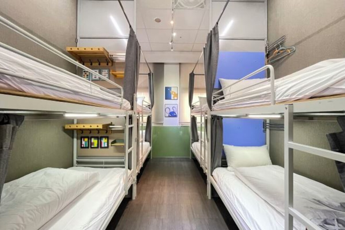A dormitory-style room with bunk beds, a wooden shelf, and a wall-mounted TV.