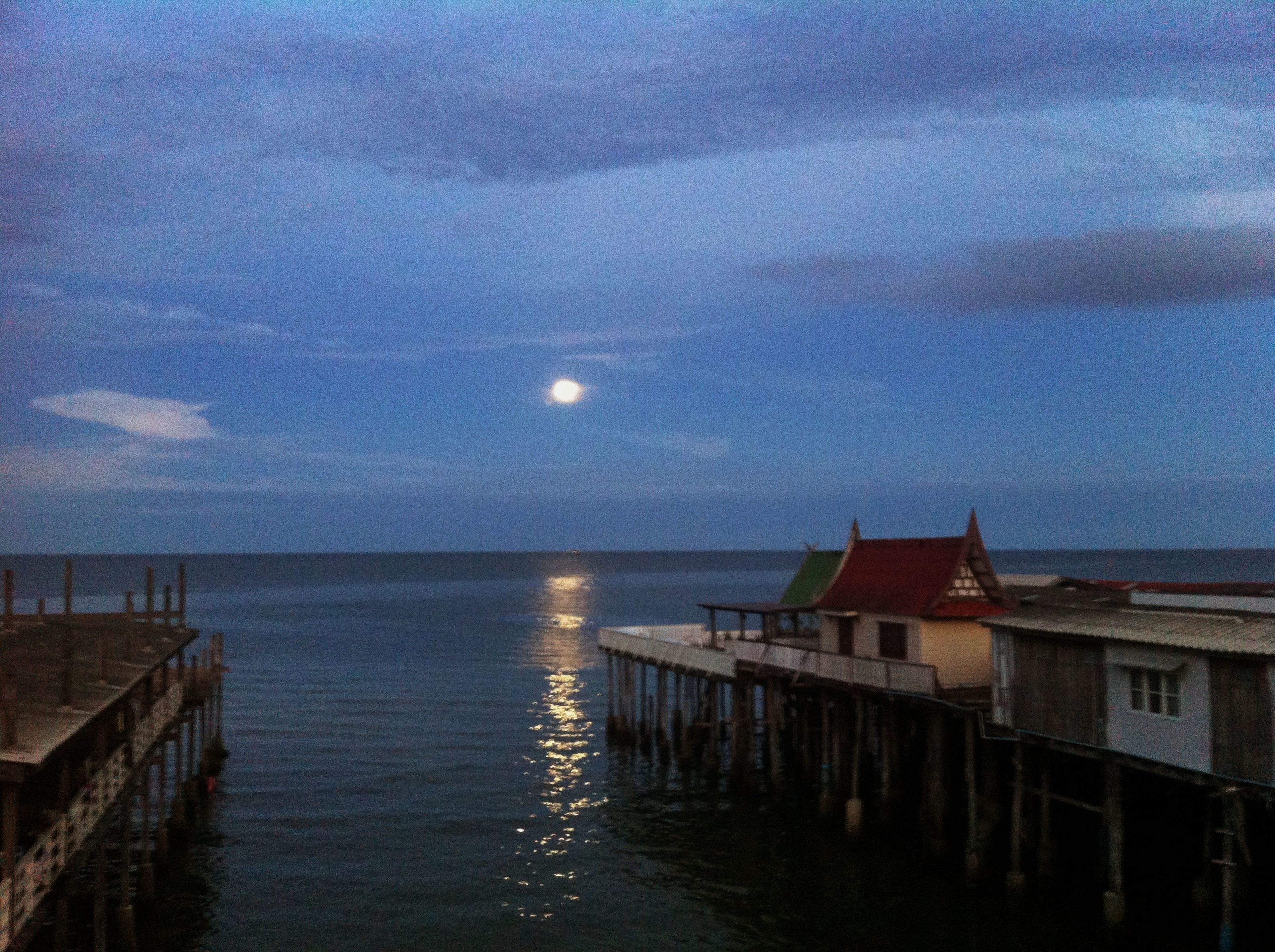 A pier extending into calm waters with a moon in the sky.