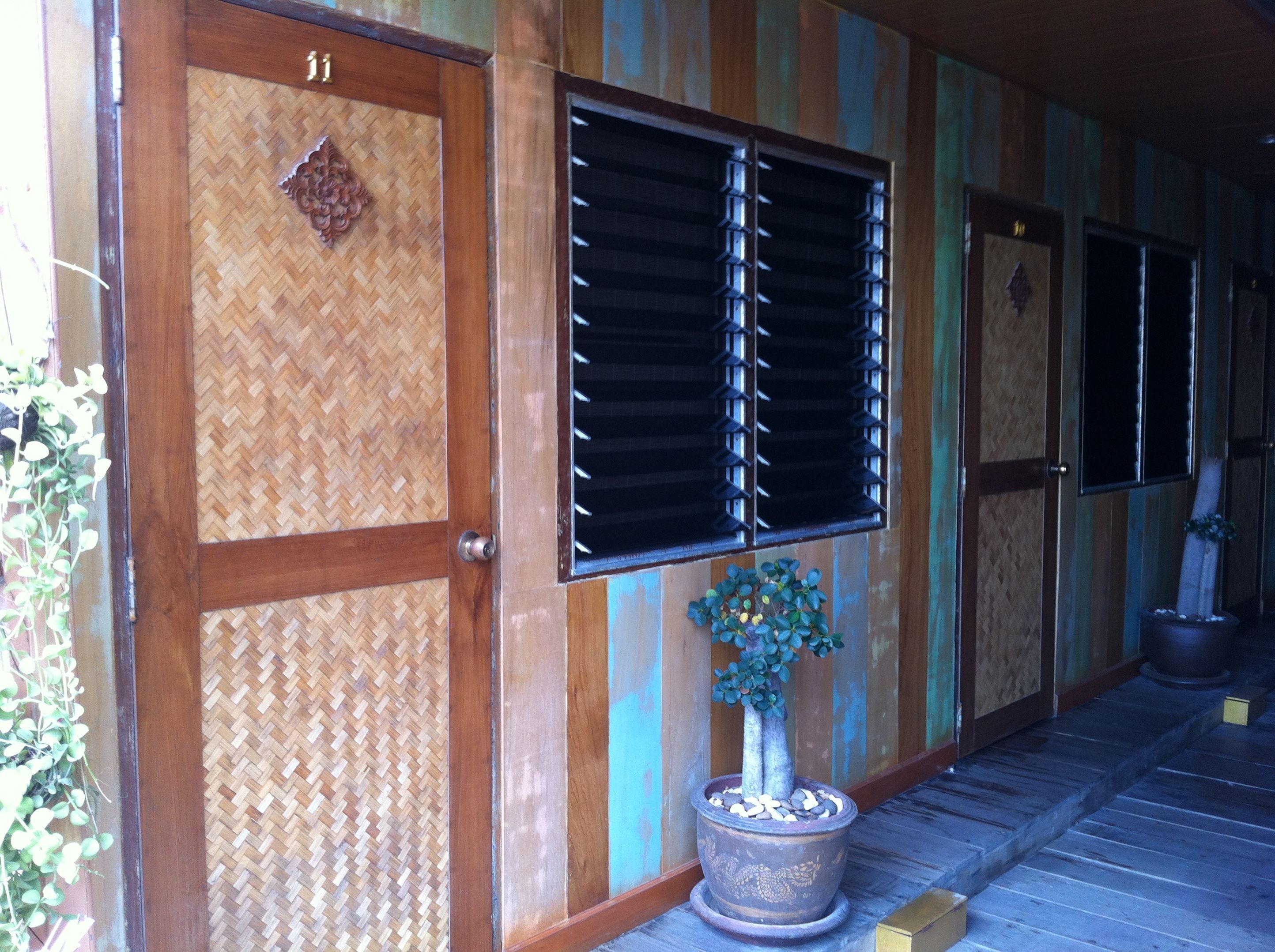 A traditional wooden building with a woven door, a potted plant, and a wooden floor. - Sukkasem Homestay (Hua Hin)
