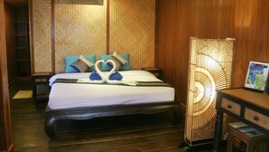 A hotel room with a large bed, a nightstand, a desk with drawers, a wall-mounted air conditioner, and a decorative lamp. - Sukkasem Homestay (Hua Hin)