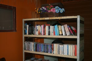 A book exchange shelf with multiple books and a floral arrangement. - Sukkasem Homestay (Hua Hin)