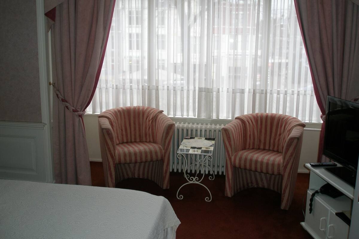 Habitación de hotel con dos sillones a rayas, una mesita, un radiador y un televisor sobre un mueble.
