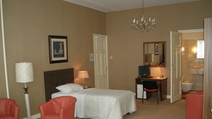 Ein Hotelzimmer mit zwei Betten, einem Schreibtisch mit Computer, einem Sessel, einer Lampe und einem Kronleuchter.