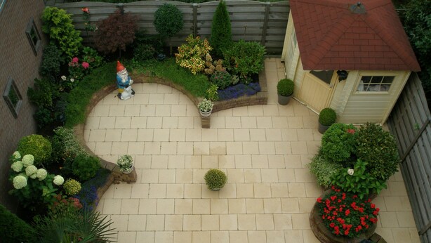 Ein Innenhof mit Pflasterweg, umgeben von verschiedenen Blumentöpfen und Blumen.