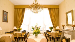 Ein formeller Speisesaal mit einer Chandelüster, gedeckten Tischen und großen Fenstern mit Vorhängen.