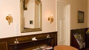 Ein Zimmer mit zwei Sesseln, einem kleinen runden Tisch, einem Spiegel, einer Chandelier und einer Tür.