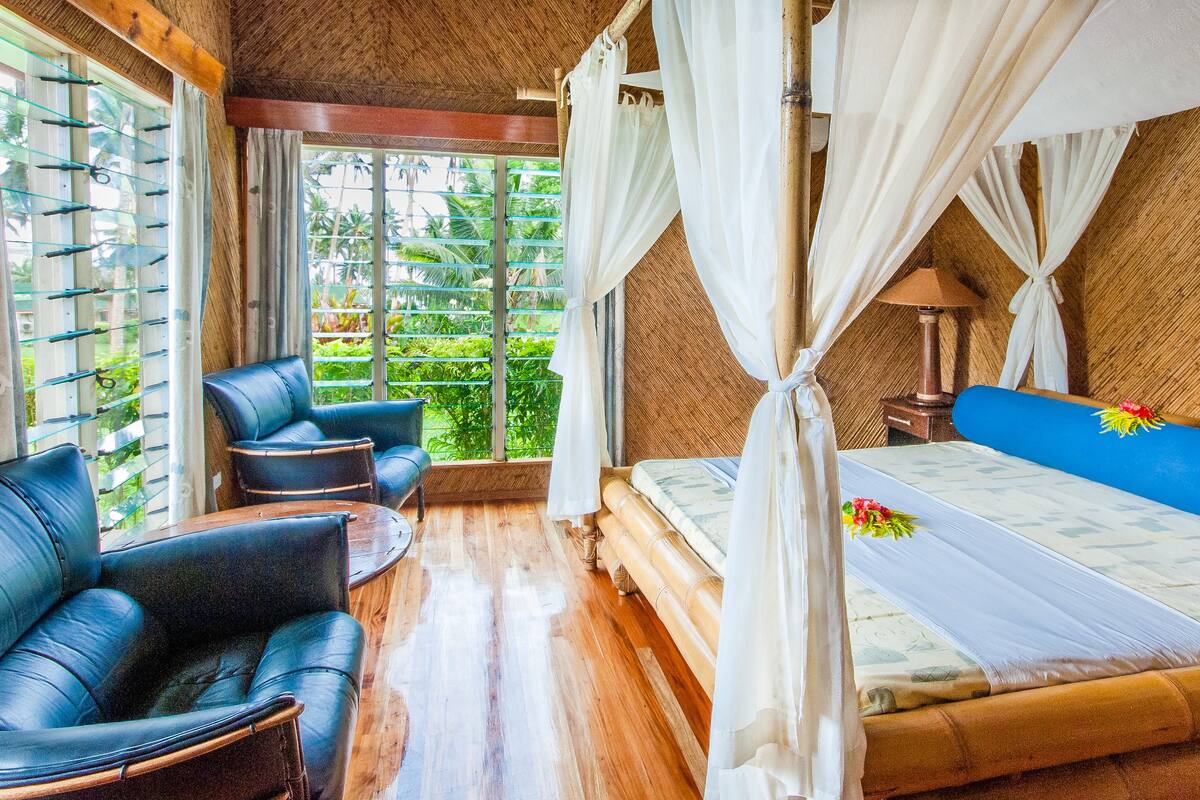 A room with a bed, a sofa, and a chair, with a view of greenery outside.