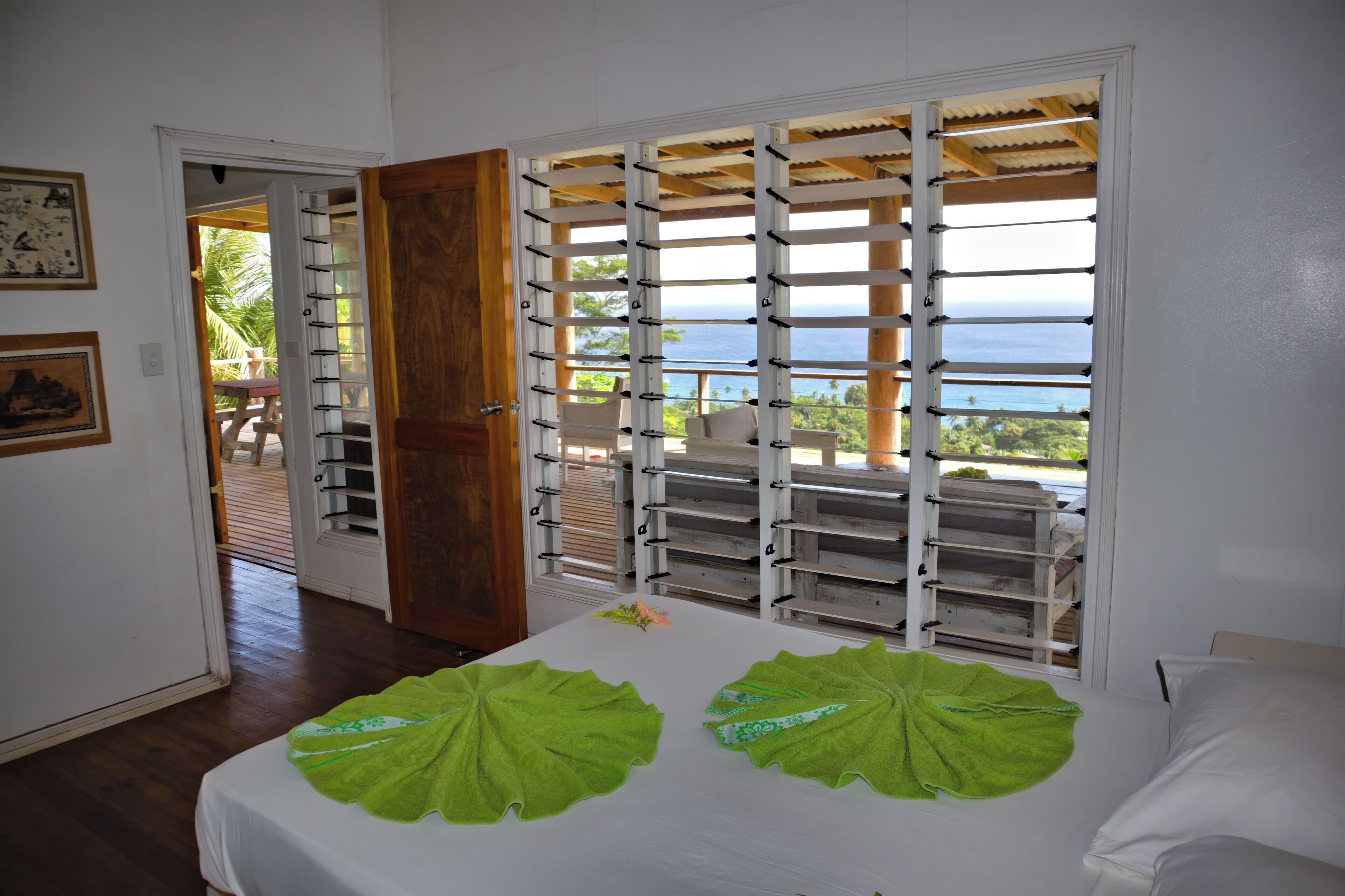 A room with a bed, a view of the ocean, a wooden door, and a balcony with outdoor furniture.