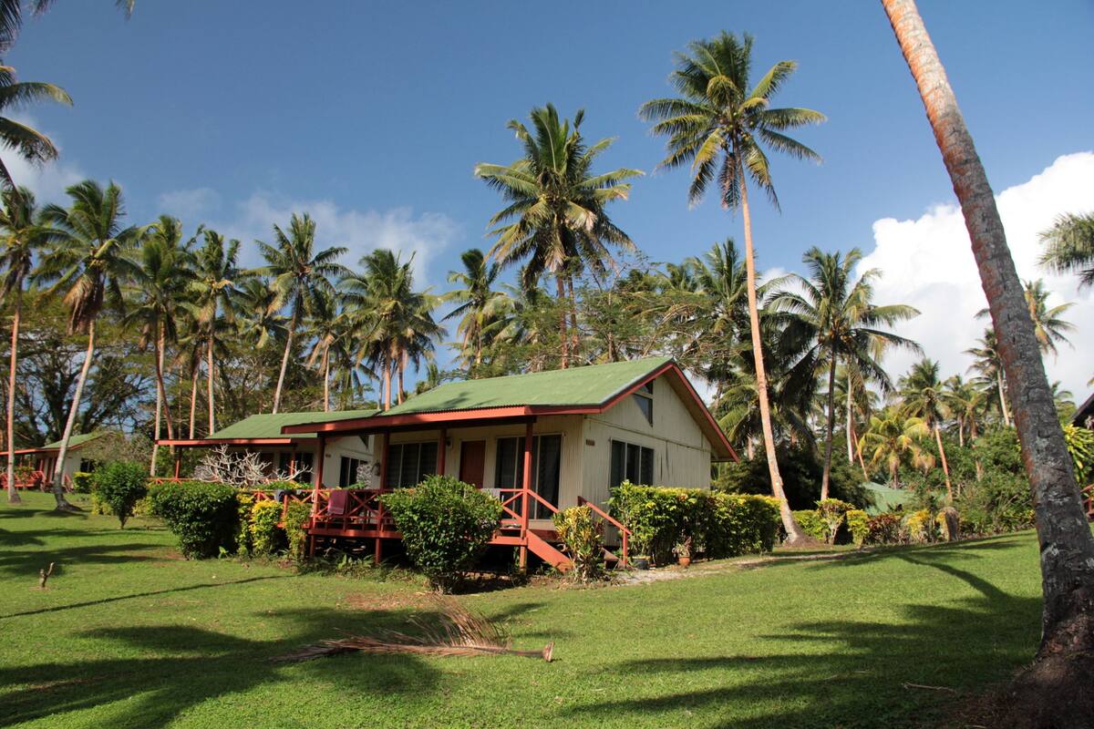 A house with a green roof and red accents, surrounded by lush greenery and palm trees.