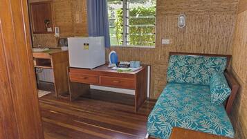 Une chambre de taille modeste, comprenant un lit, un bureau, un réfrigérateur et une fenêtre donnant sur un espace verdoyant.