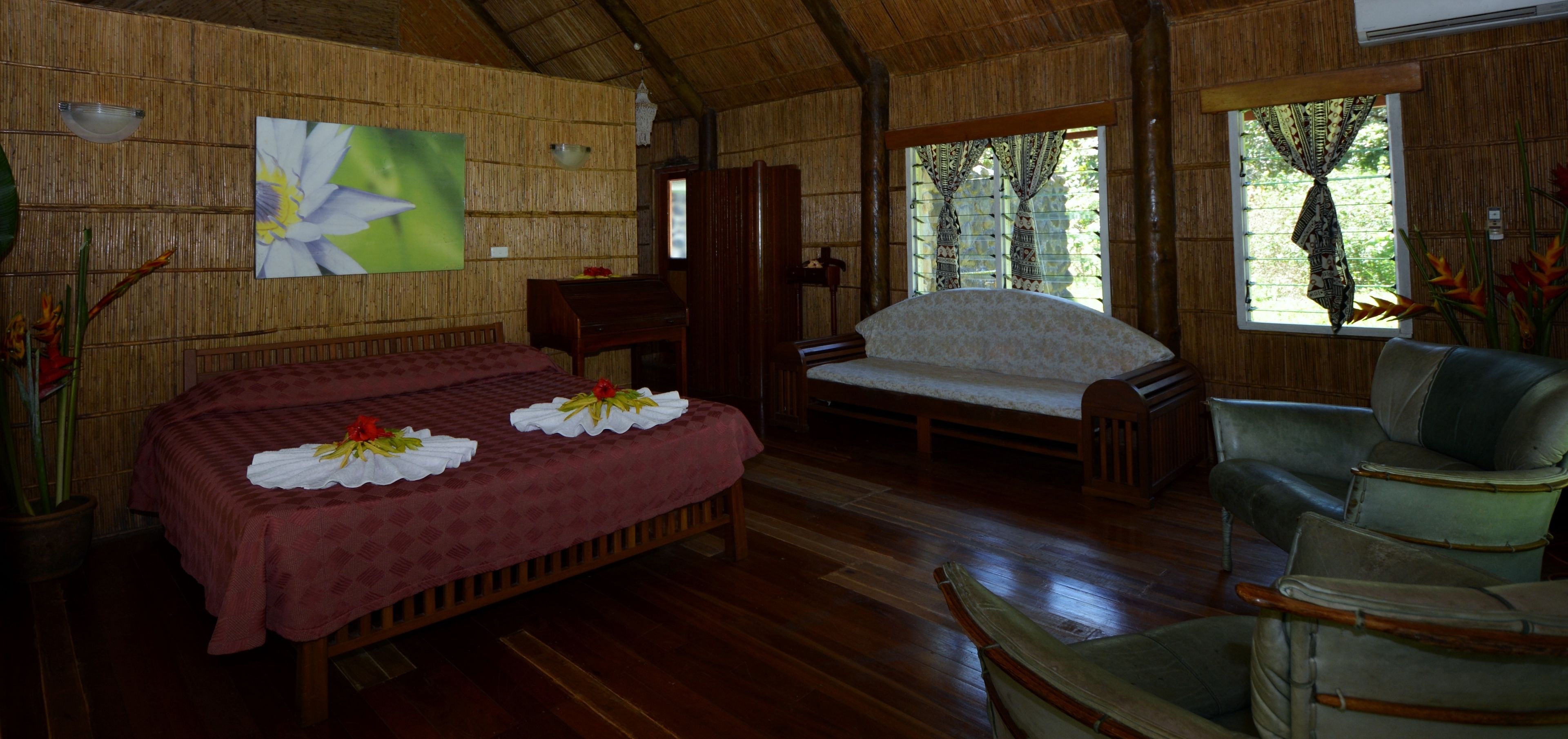 A room with a bed, a sofa, and a chair. There is a painting on the wall and a window with curtains.