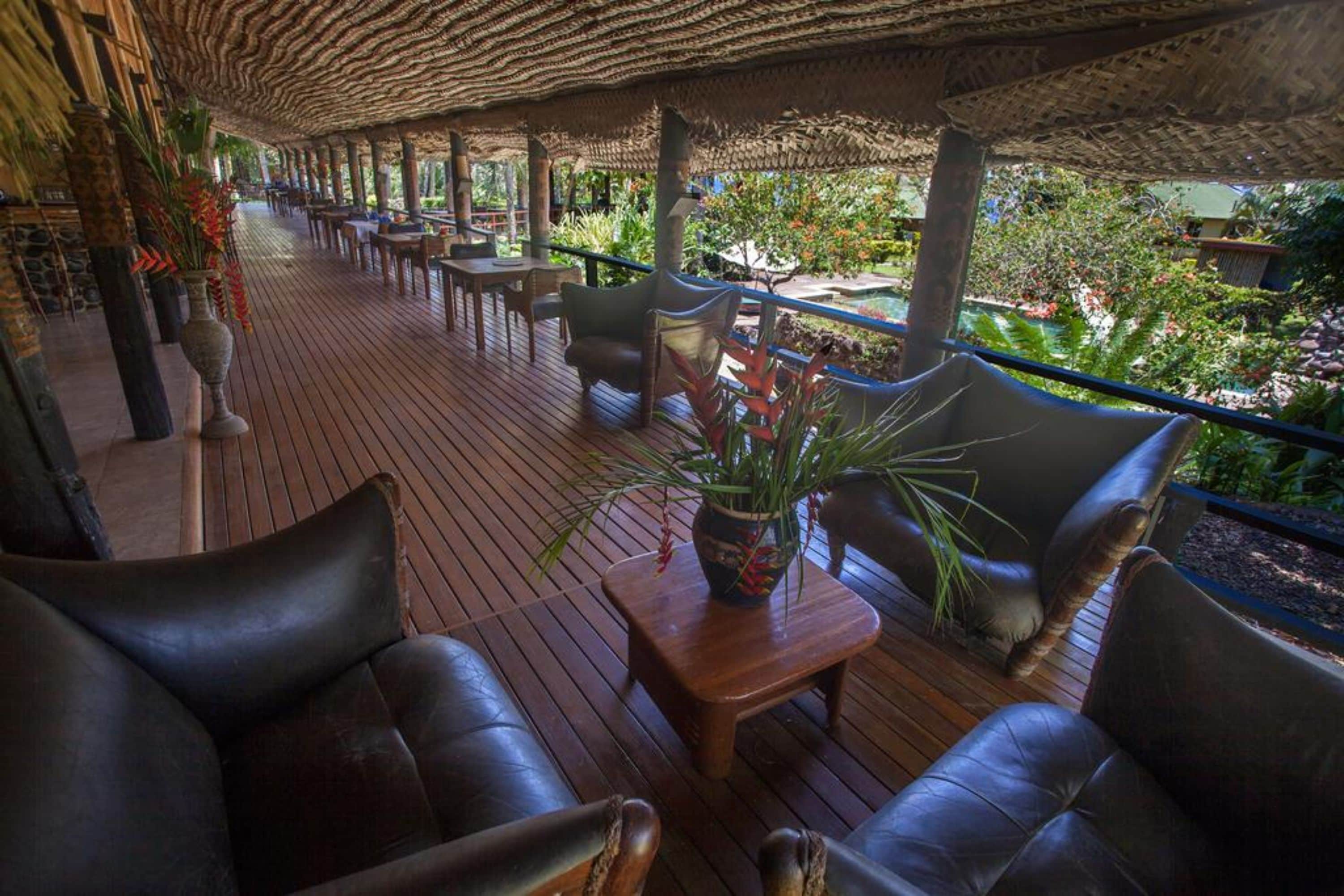 Un espacio al aire libre cubierto con suelo de madera, sillas de cuero y una planta en maceta sobre una mesa.