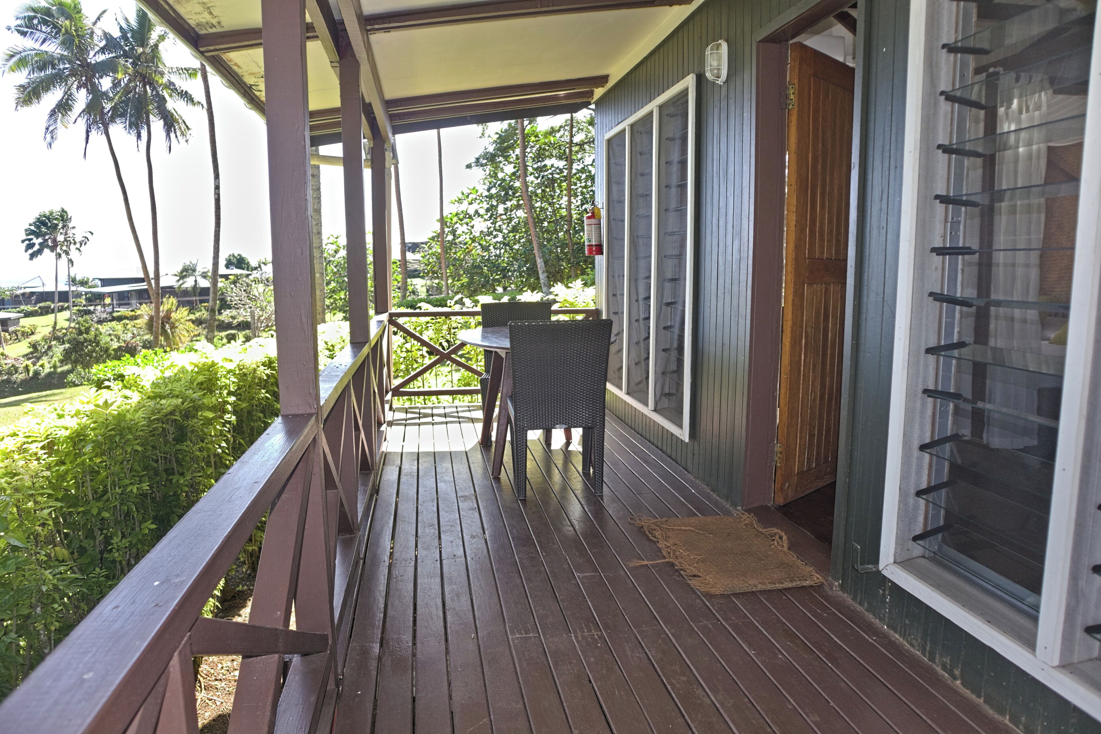 A wooden deck with a table and chairs, a window with blinds, and a door.
