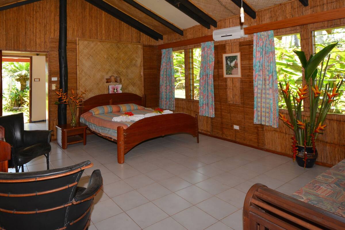 A wooden room with a bed, a desk, a chair, and a large window with curtains.