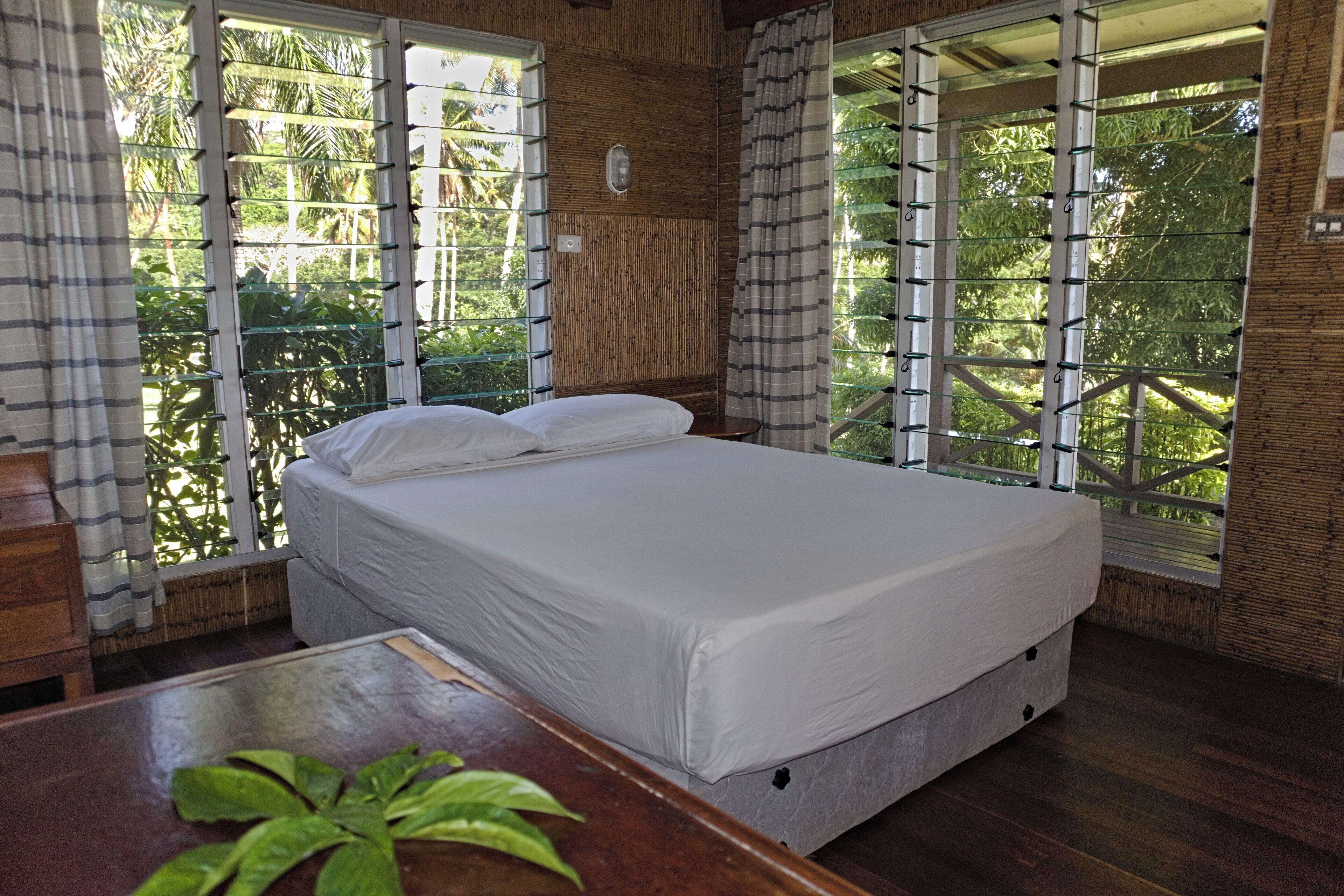 A bedroom with a bed, a wooden table, and large windows with curtains.