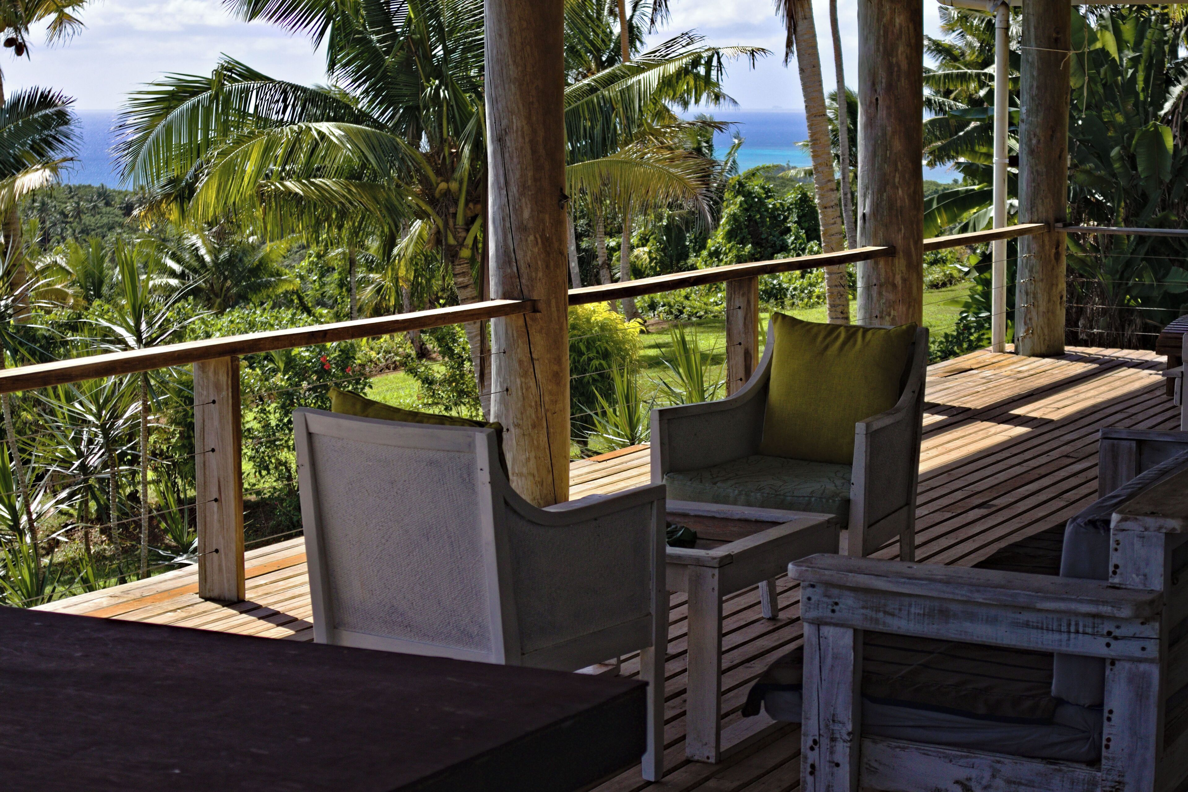 A wooden deck with seating, overlooking a lush landscape and the ocean.