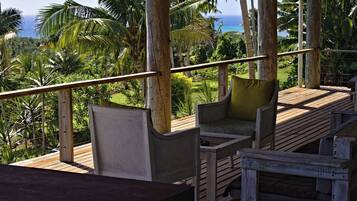 A wooden deck with seating, overlooking a lush landscape and the ocean.