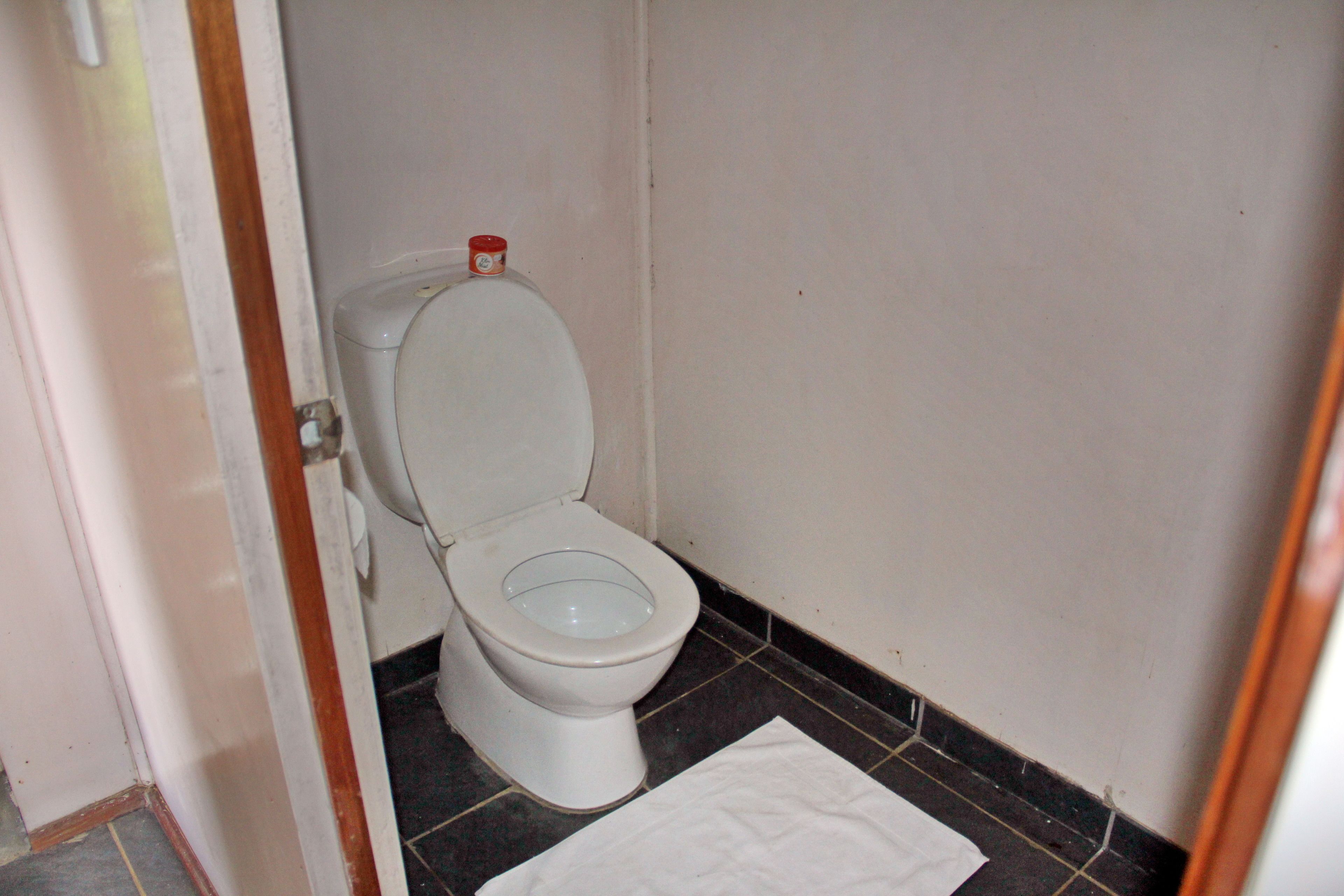 Un baño pequeño y limpio, con inodoro blanco, un tapete blanco en el suelo y un recipiente rojo en la pared.