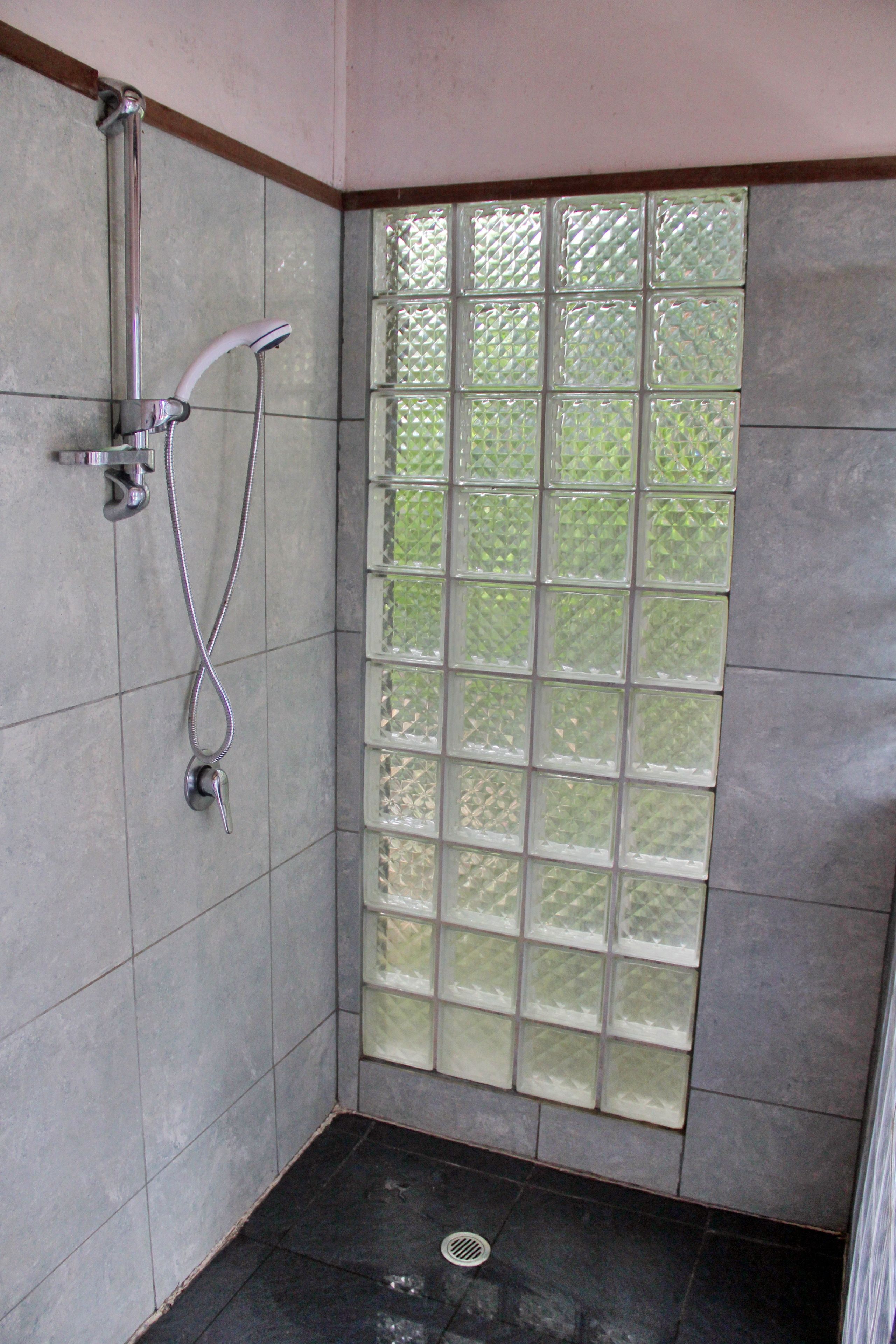 A shower with a glass door, a metal showerhead, and a drain on the floor.