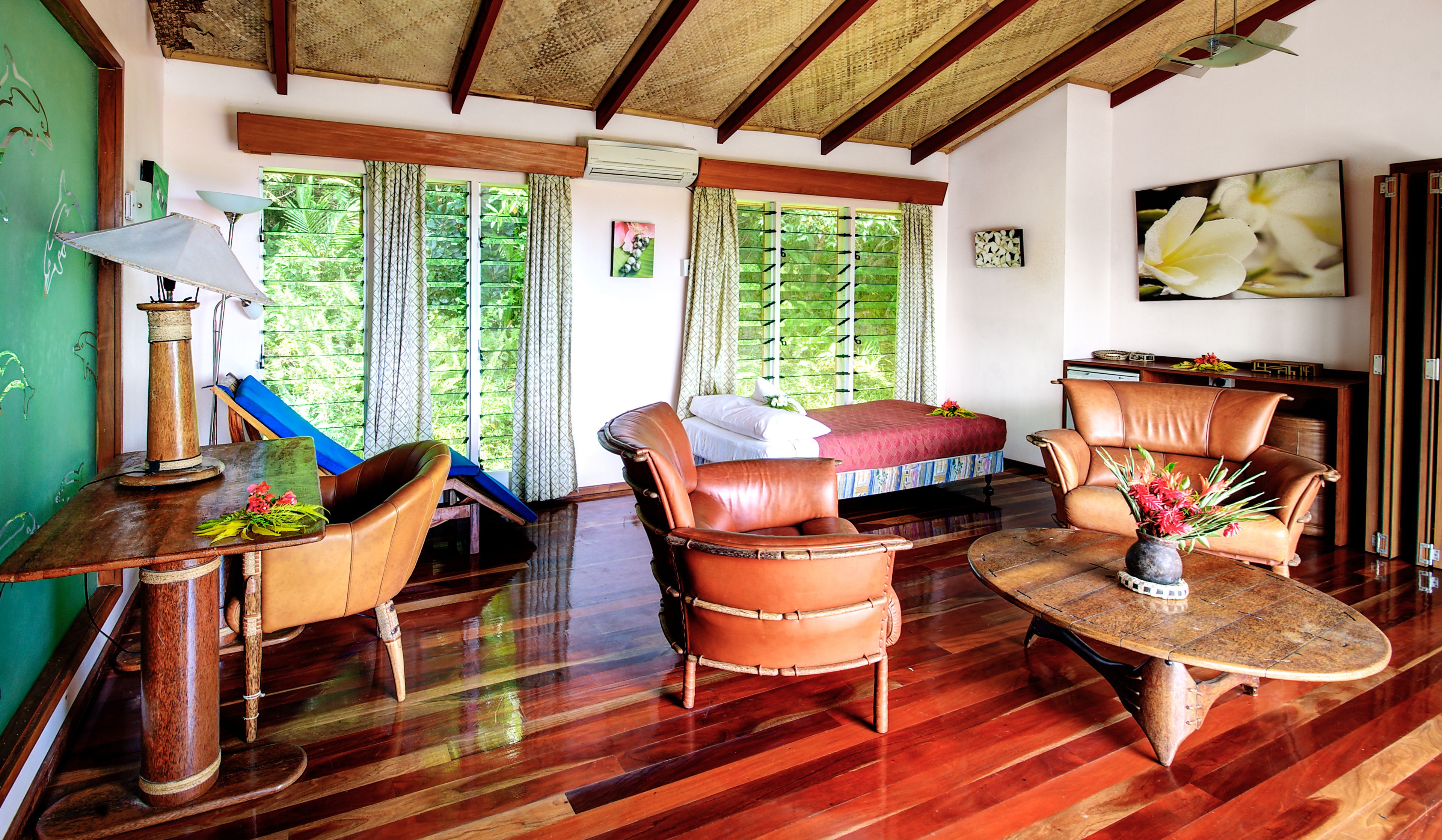 A room with a bed, two leather chairs, a table, and a lamp.