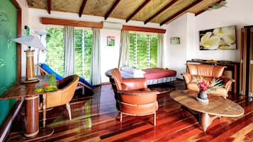 A room with a bed, two leather chairs, a table, and a lamp.