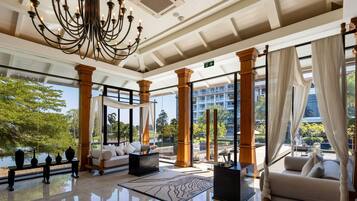 A spacious lobby with a chandelier, seating area, and large windows offering views of greenery and a building.