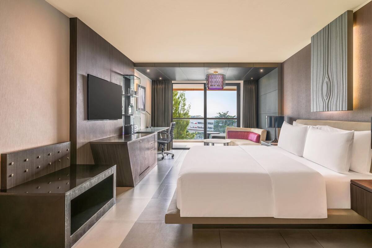 A modern hotel room with a large bed, a TV, a desk, and a view of the city.