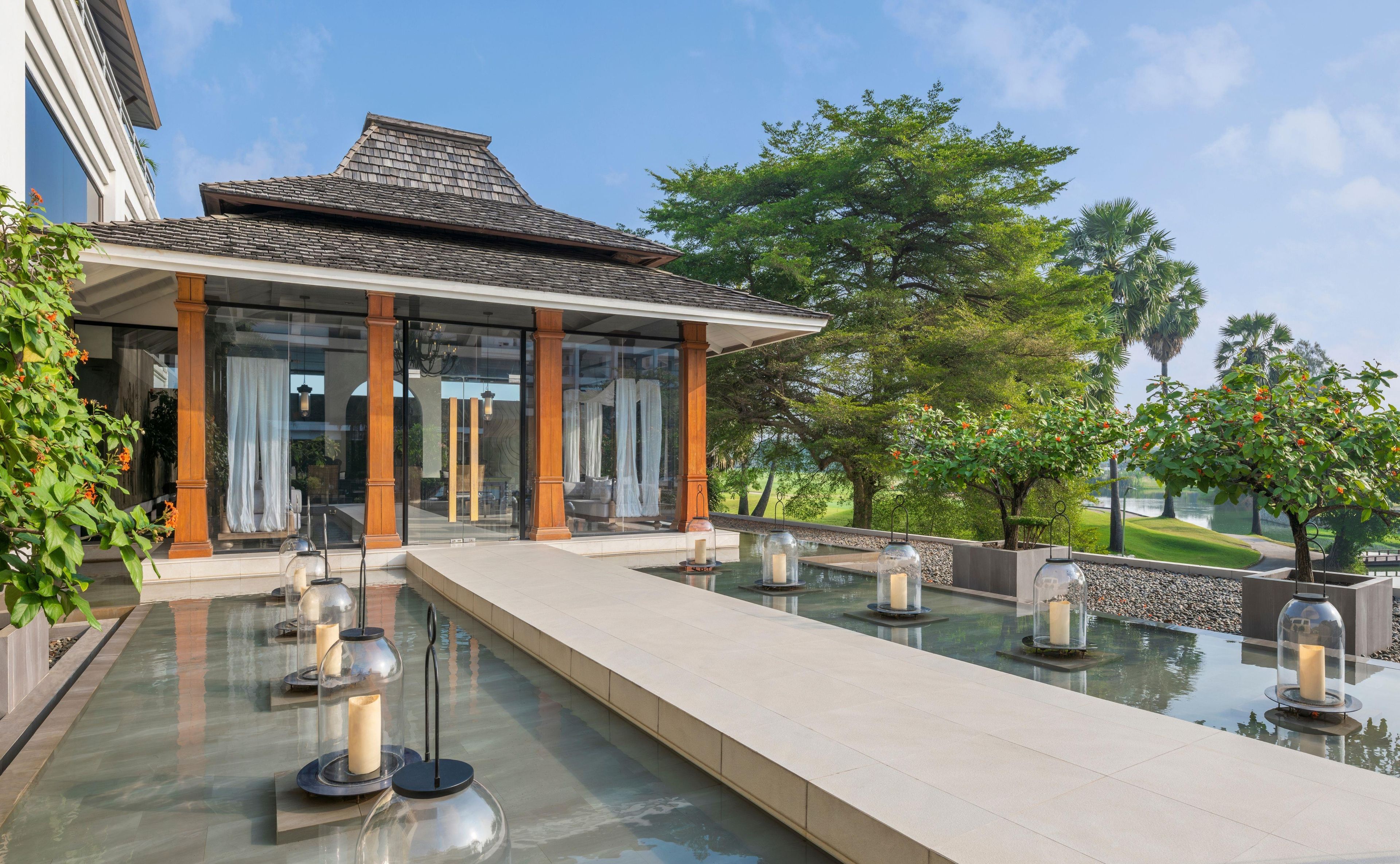 A modern building with a covered patio, a reflective pool, and outdoor lighting fixtures.