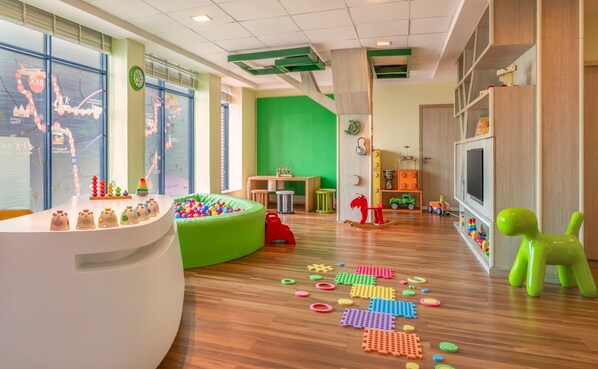 A children's play area with a green wall, wooden flooring, and various toys and play structures. - Hilton Bangkok Suvarnabhumi Golf Resort & Spa (Bang Phli)