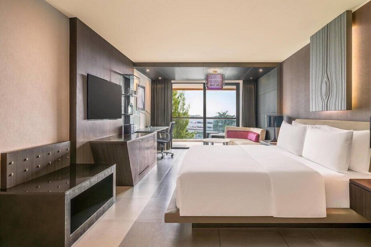 A modern hotel room with a large bed, a desk, a TV, and a balcony with a city view.