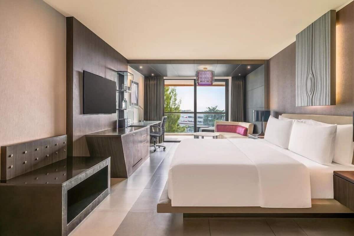 A modern hotel room with a large bed, a desk, a TV, and a balcony with a city view.