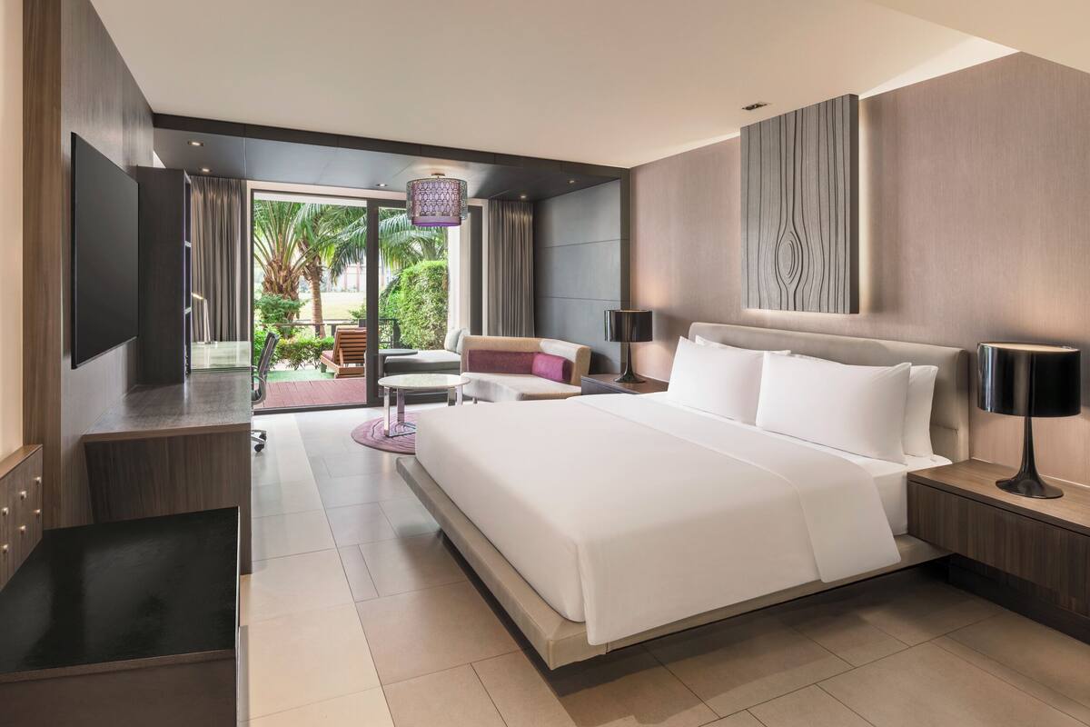 A modern hotel room with a large bed, a TV, a desk, and a view of the outdoors.