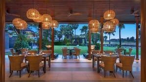 A restaurant with wicker furniture and hanging lights, overlooking a well-maintained lawn and distant golf course. - Hilton Bangkok Suvarnabhumi Golf Resort & Spa (Bang Phli)