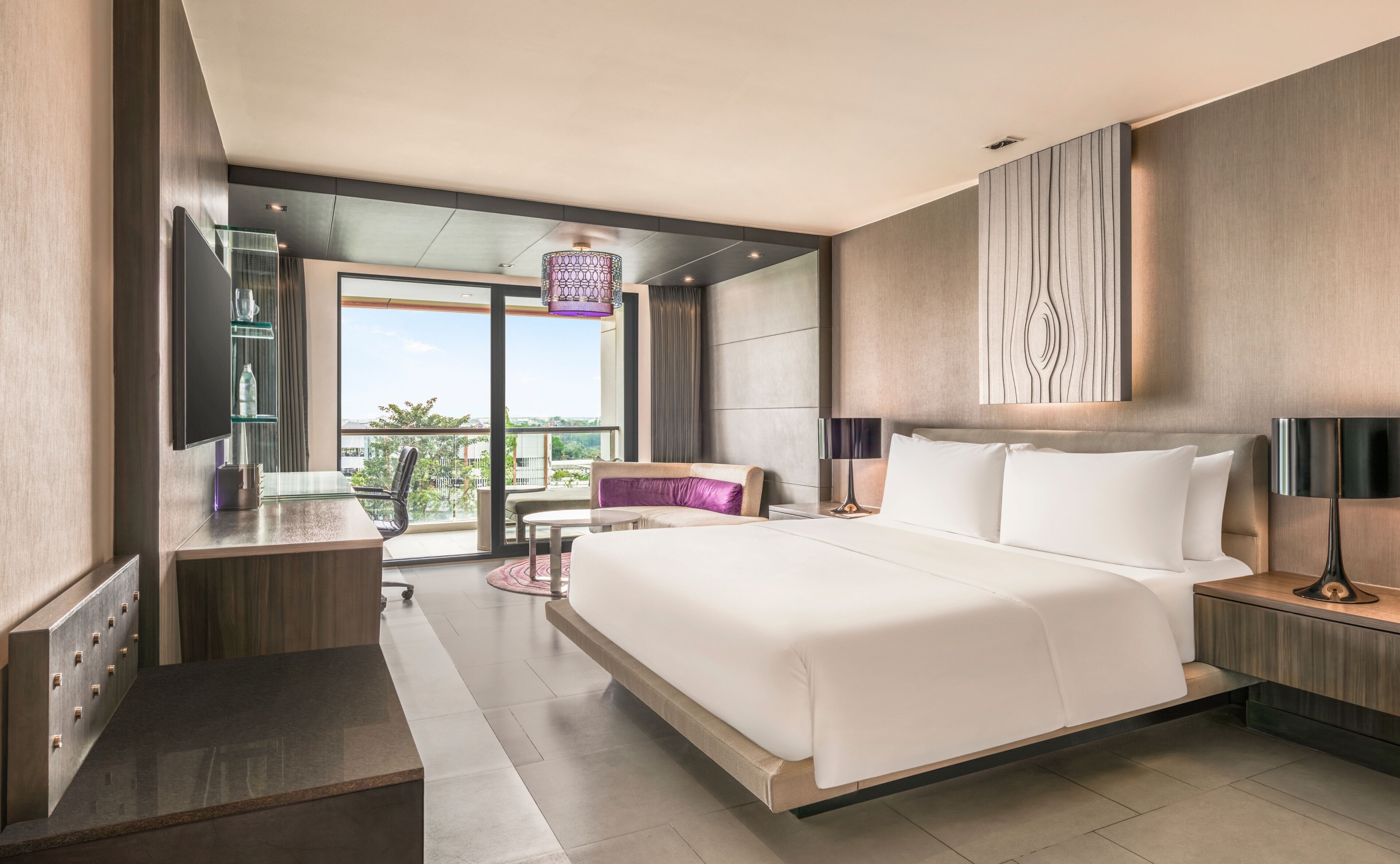 A modern hotel room with a large bed, a desk, a chair, and a view of the outdoors.