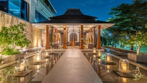 A covered outdoor seating area with a reflective floor, surrounded by potted plants and a view of a building. - Hilton Bangkok Suvarnabhumi Golf Resort & Spa (Bang Phli)