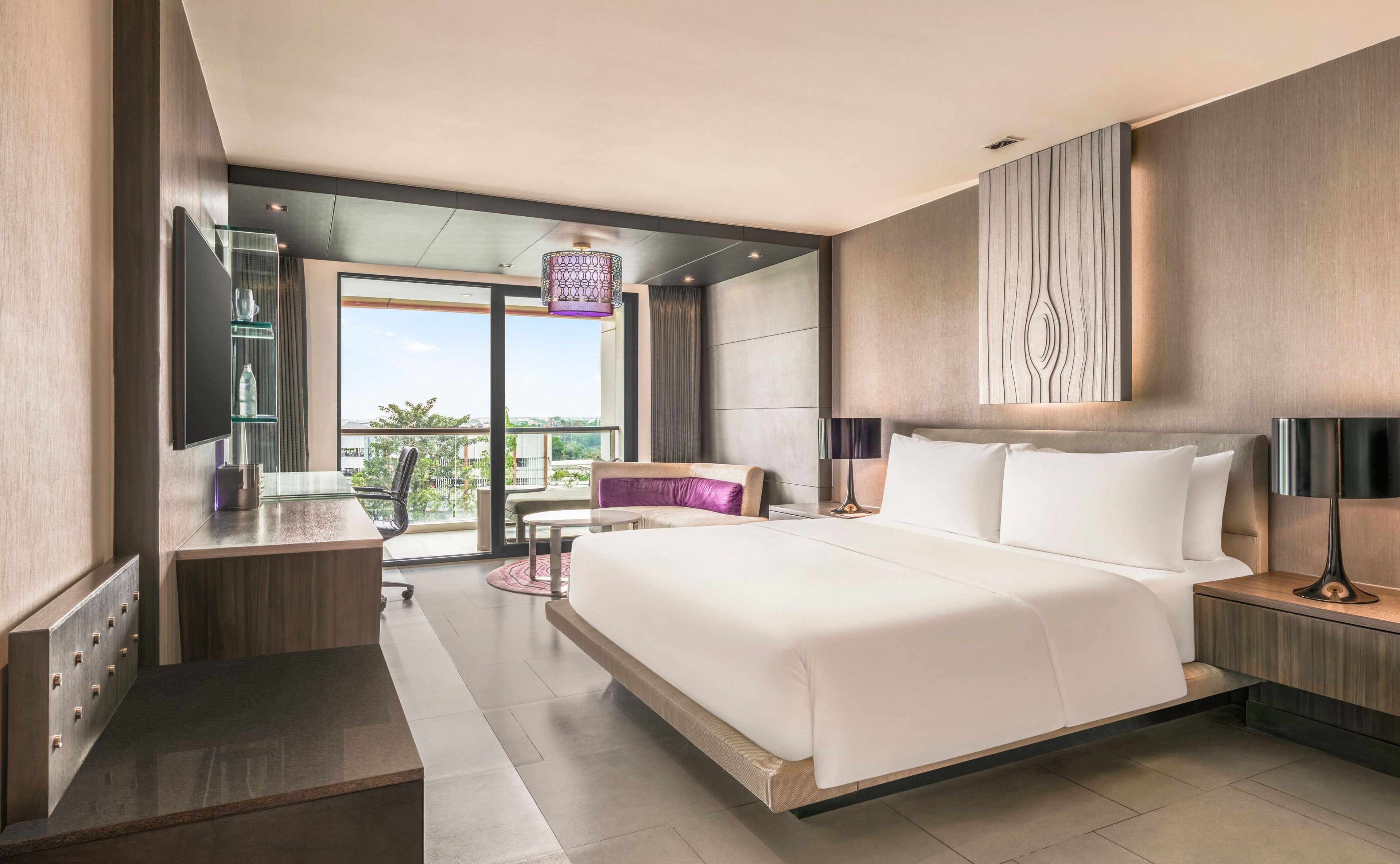 A modern hotel room with a large bed, a desk, a chair, and a view of the outdoors.