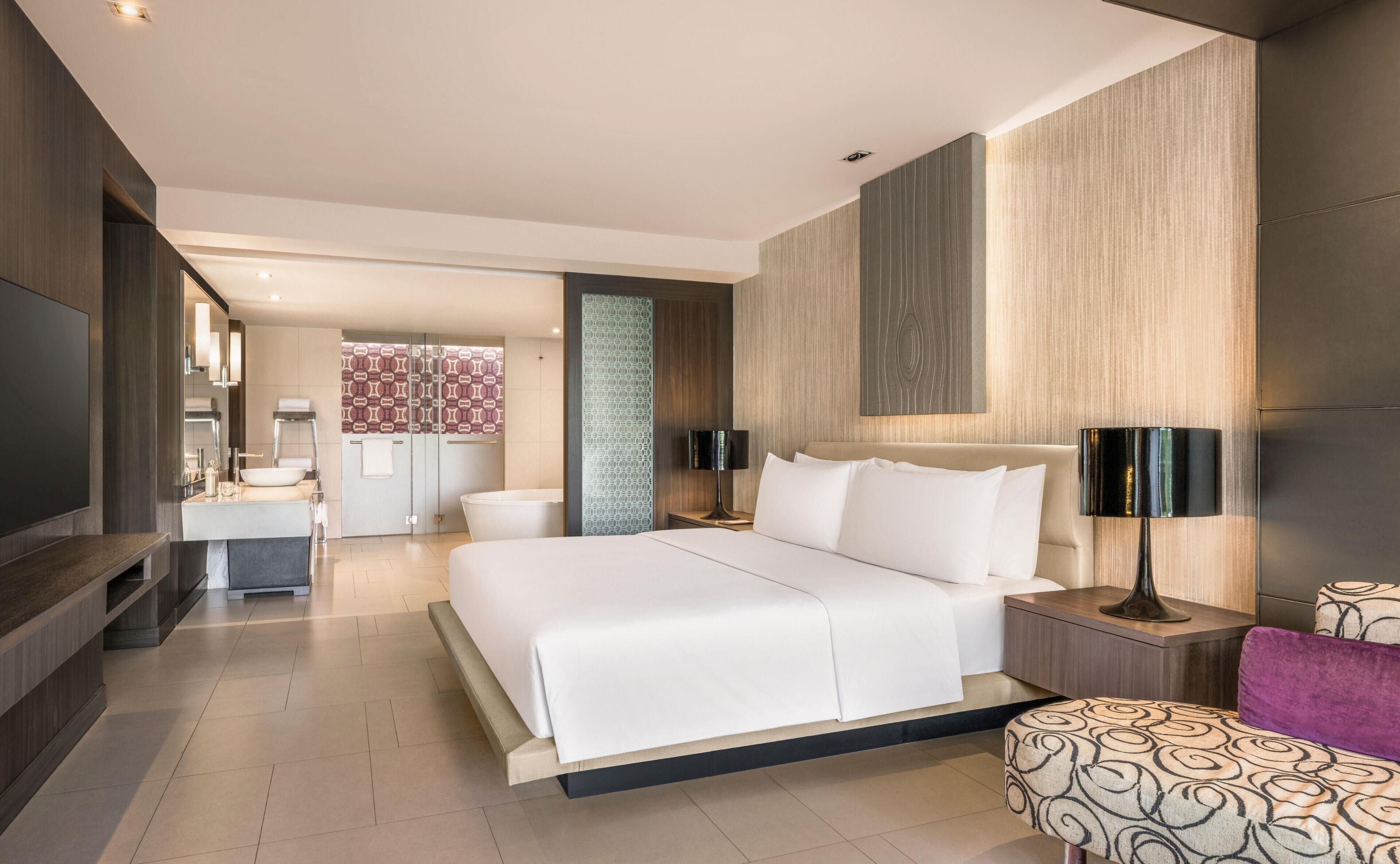 A modern hotel room with a large bed, bedside tables, a TV, and a bathroom with a shower and toilet.