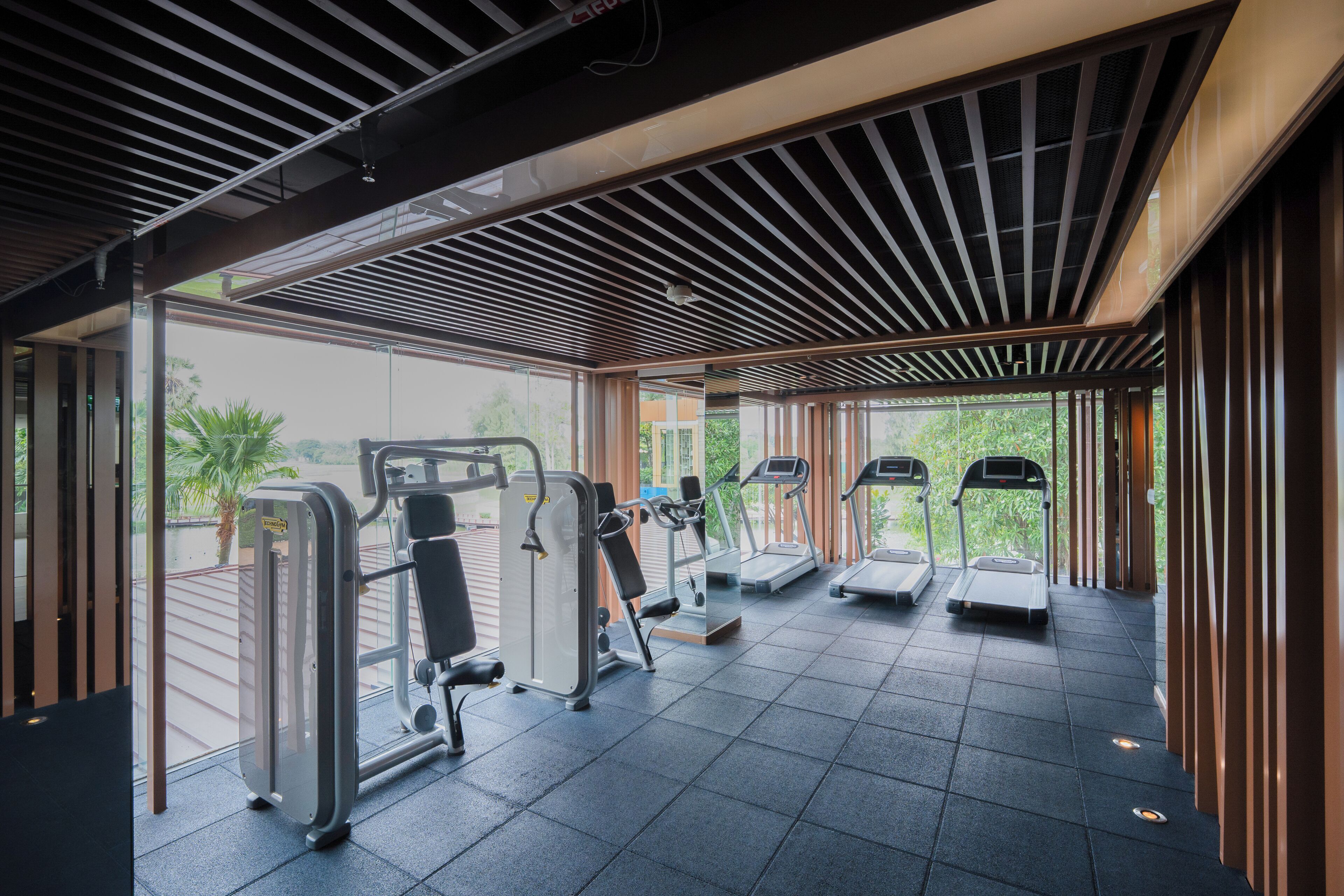 A gym with exercise equipment, large windows, and a view of greenery.