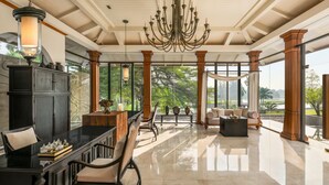 A spacious lobby with a grand chandelier, a black dining table with chairs, a sofa, and a view of greenery outside. - Hilton Bangkok Suvarnabhumi Golf Resort & Spa (Bang Phli)