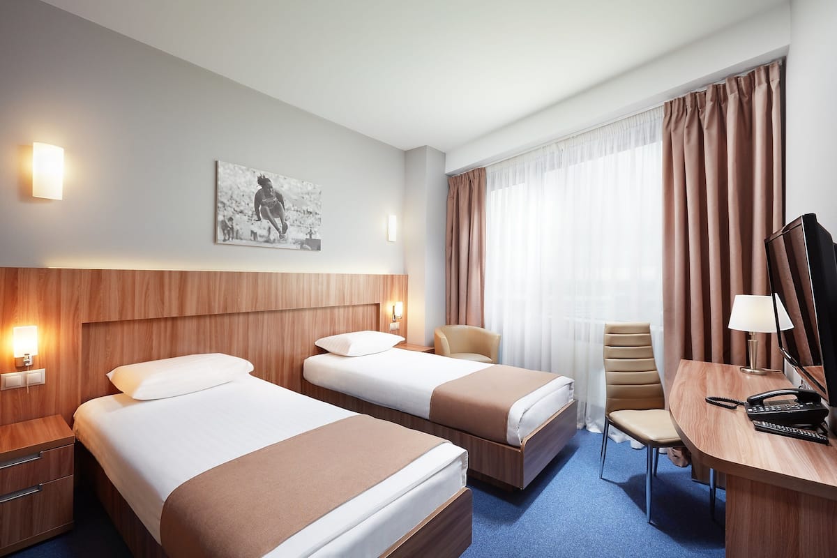 A hotel room with two beds, a desk with a lamp, a chair, and a painting on the wall.