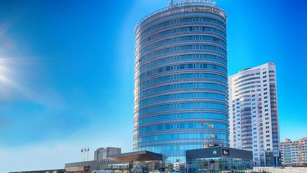 A modern hotel with a curved facade, multiple floors, and a prominent entrance with a glass facade. - Slavyanskaya Hotel (Minsk)