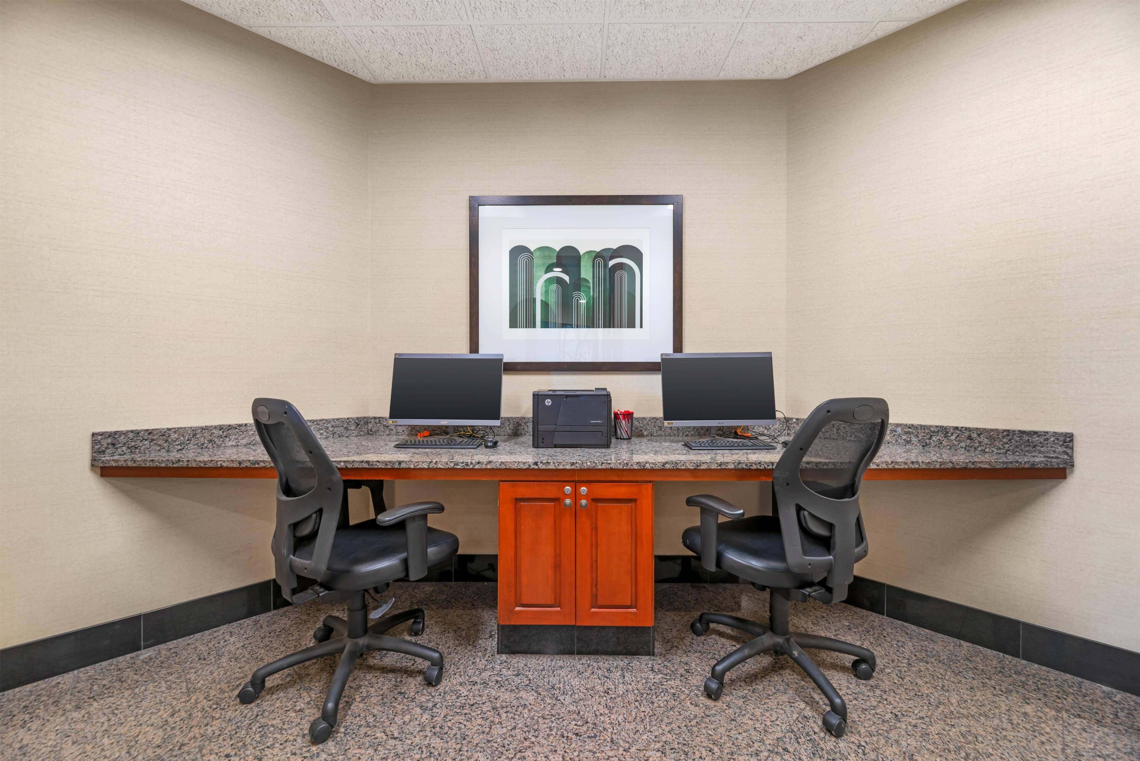 Une salle de conférence avec une table en granit, deux chaises de bureau noires, un meuble en bois et une œuvre d’art encadrée au mur.