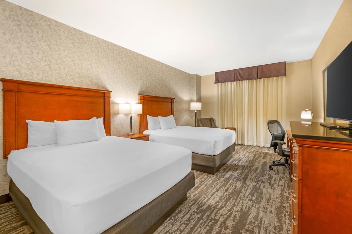 Habitación de hotel con dos camas, un escritorio, una silla y un televisor.