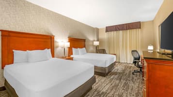 A hotel room with two beds, a desk, a chair, and a television.