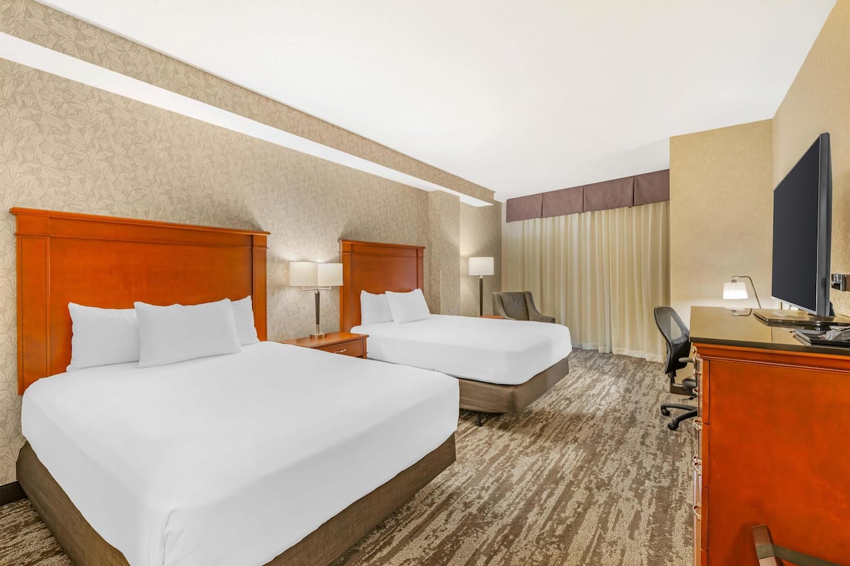Habitación de hotel con dos camas, un escritorio, una silla, un televisor y una ventana con cortinas.