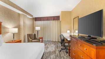 Habitación de hotel con una cama grande, un escritorio con televisor de pantalla plana, una silla, un aparador y una ventana con cortinas.
