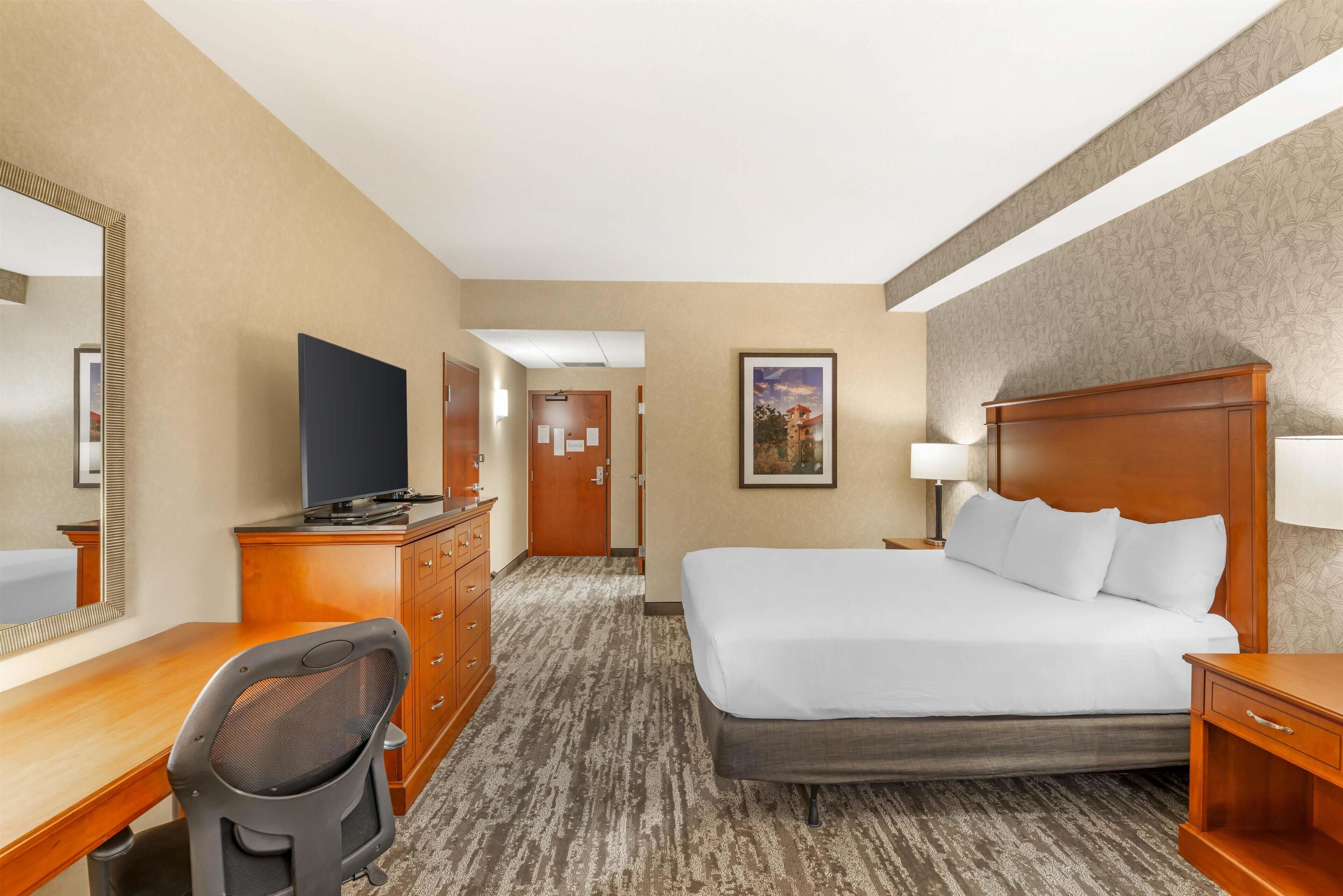Una habitación de hotel con cama, escritorio, silla, cómoda y televisor.